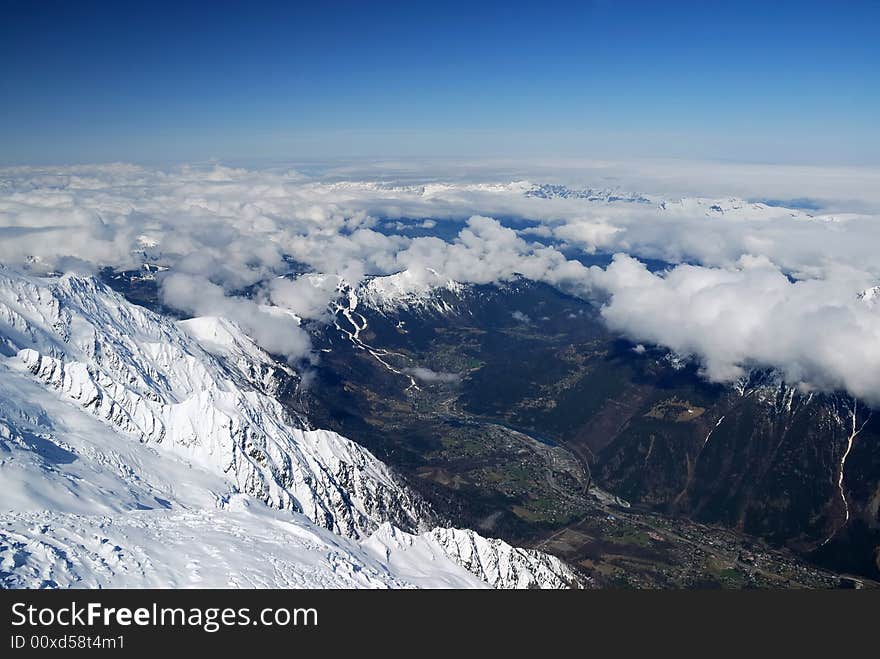 Spring valley Chamonix between high snow mountains occupied by light layer of white clouds and blue sky, view from above. Spring valley Chamonix between high snow mountains occupied by light layer of white clouds and blue sky, view from above