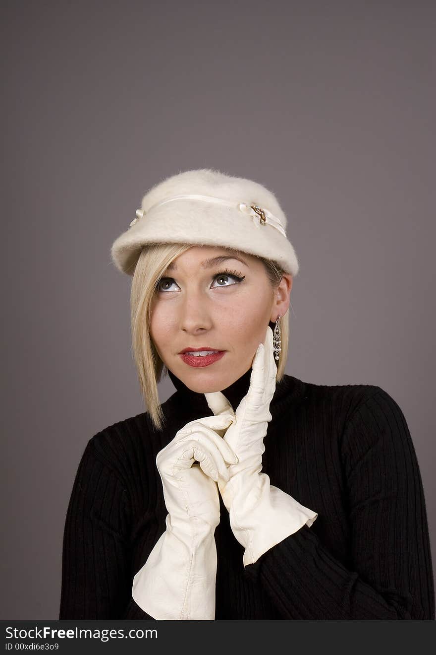 A blonde in a black fur hat and a black turtleneck with her hand on her chin looking up. A blonde in a black fur hat and a black turtleneck with her hand on her chin looking up