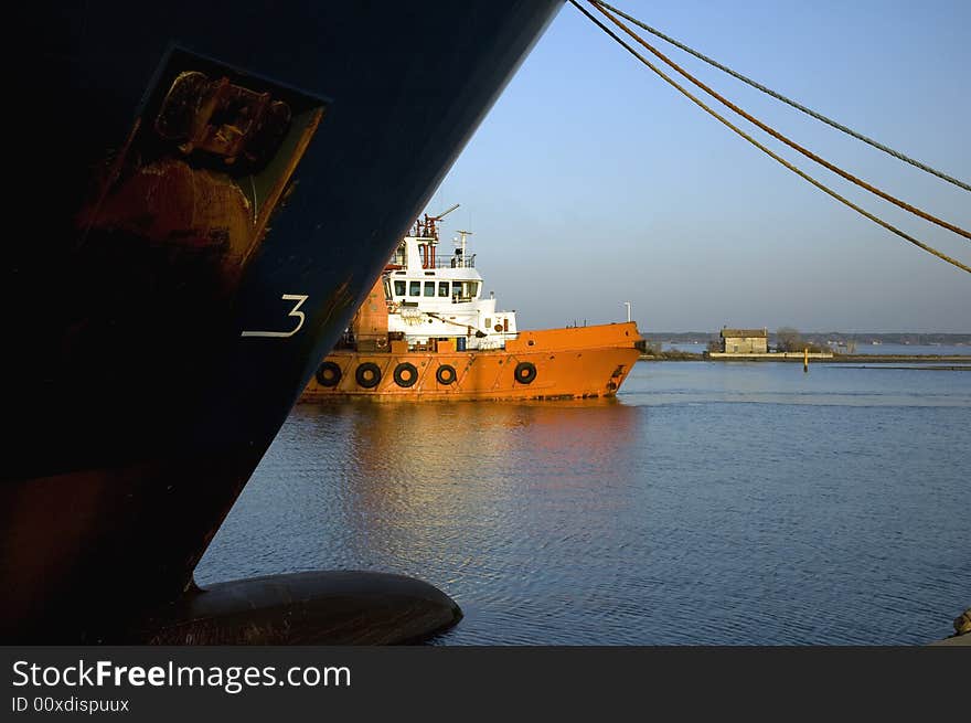 A tugboat / supply vessel slowly manouvres backwards to its bearth. A larger oceangoing vessel is bearthed at the opposite key. A tugboat / supply vessel slowly manouvres backwards to its bearth. A larger oceangoing vessel is bearthed at the opposite key.