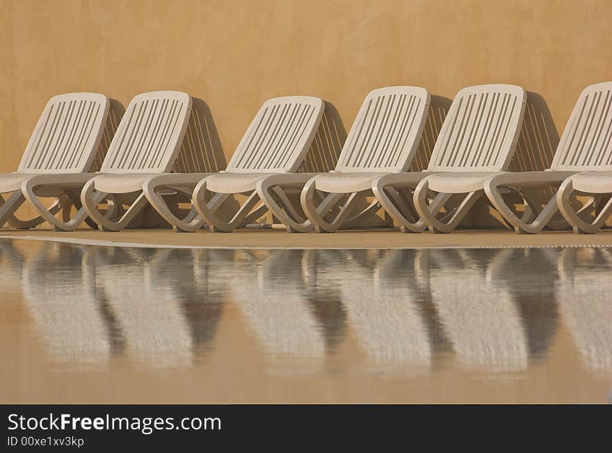 White plastic seats standing on a terrace next to a pool