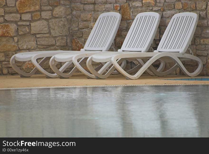 White plastic seats standing on a terrace next to a pool