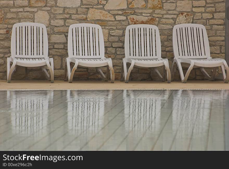 White plastic seats standing on a terrace next to a pool