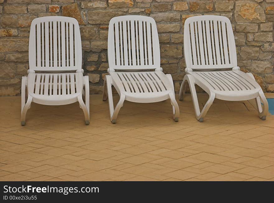 White plastic seats standing on a terrace next to a pool