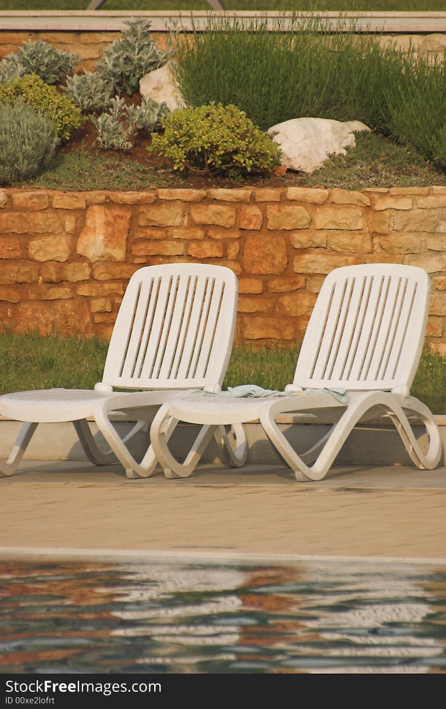 White plastic seats standing on a terrace next to a pool