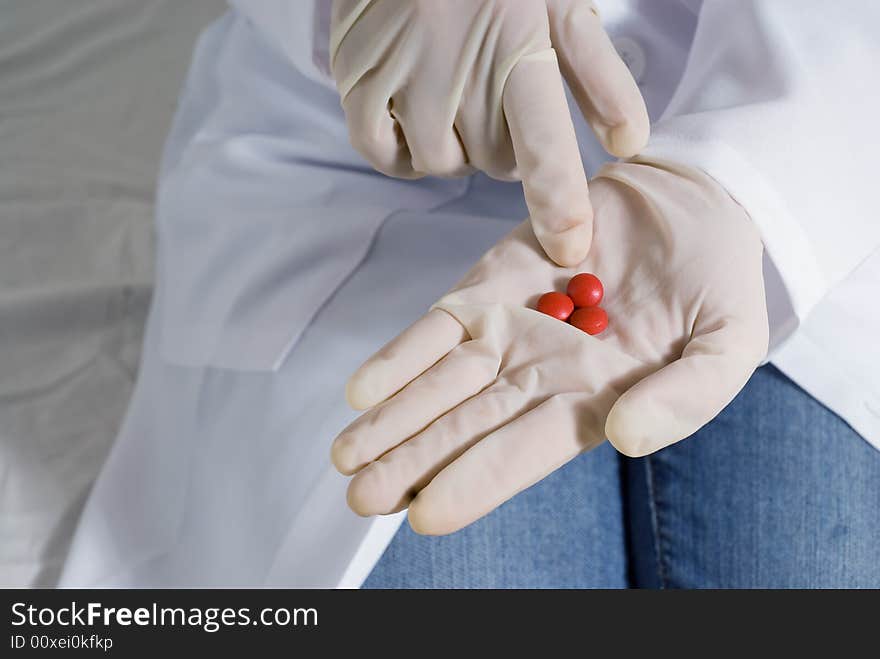 A latex gloved hand holding out pills, with the other hand pointing at them. A latex gloved hand holding out pills, with the other hand pointing at them.