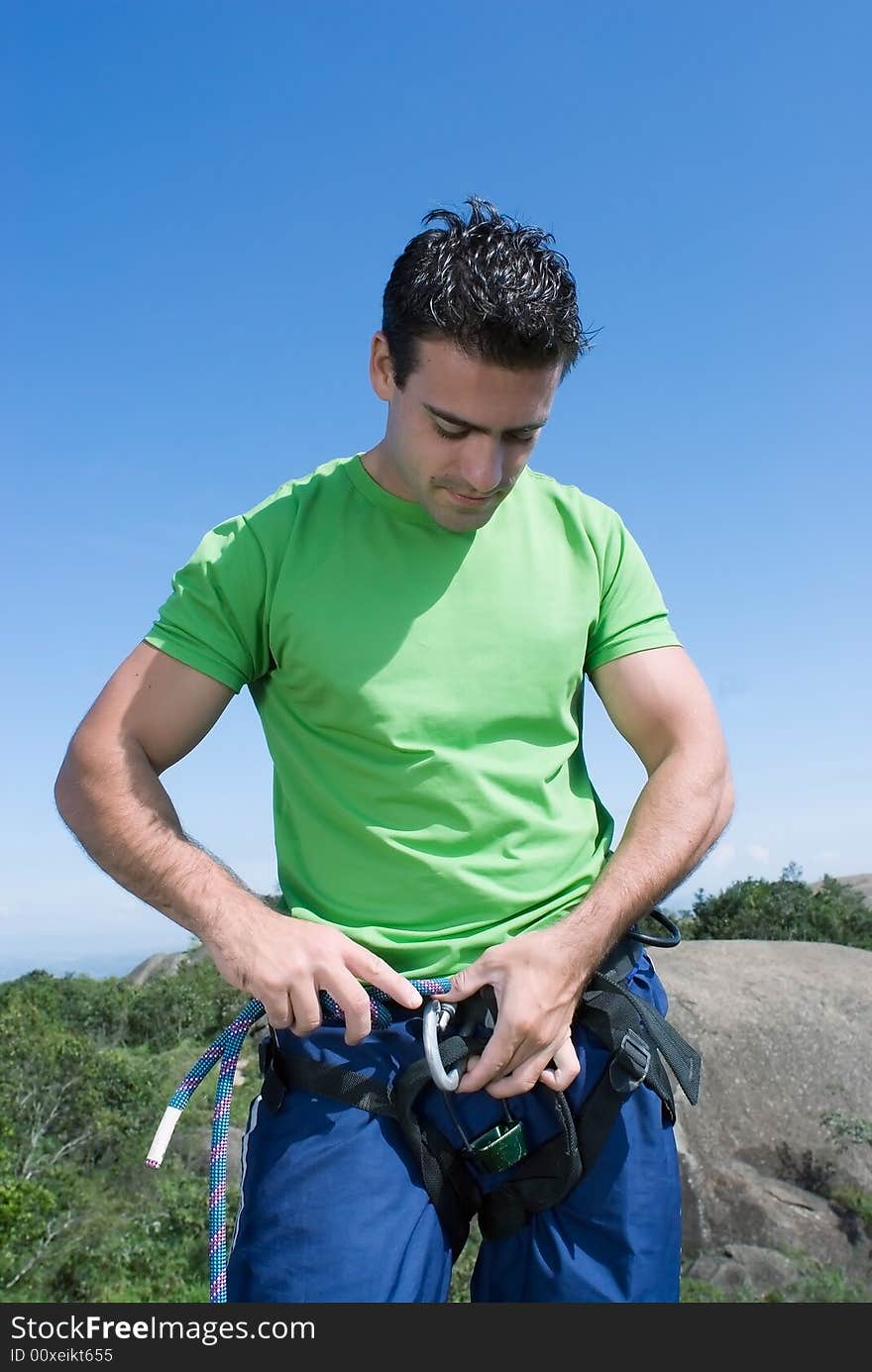 Athletic young climber checking his gear and climbing harness. Vertical shot set against a blue sky. Athletic young climber checking his gear and climbing harness. Vertical shot set against a blue sky.