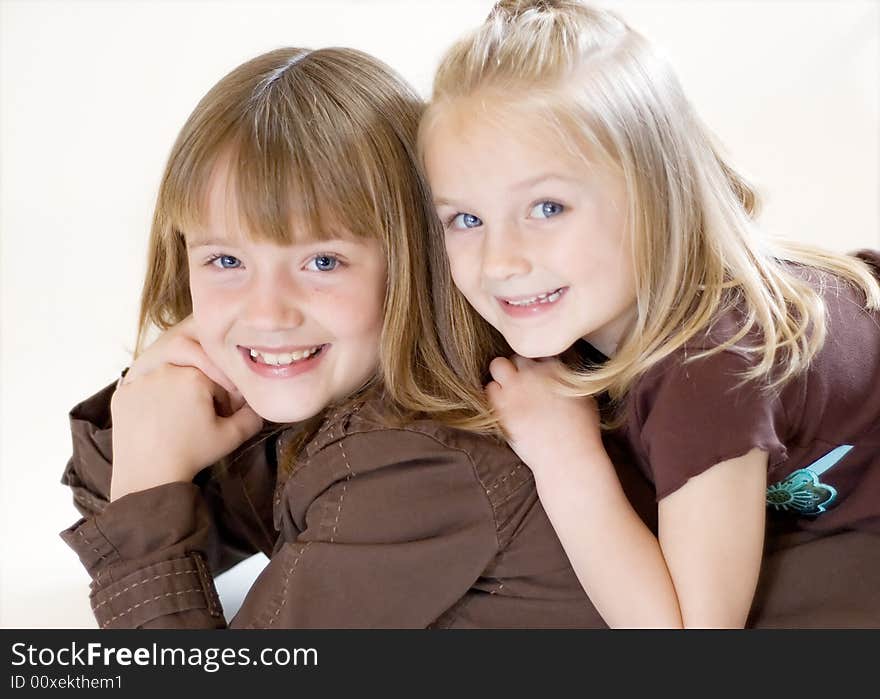 Two cute young sisters posing together in a studio. Horizontally framed shot isolated against a white studio background. Two cute young sisters posing together in a studio. Horizontally framed shot isolated against a white studio background.