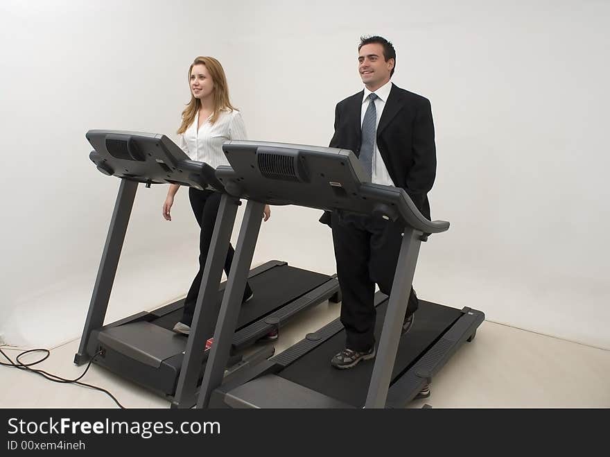 Two businesspeople (male and female) running on a treadmill and looking at each other facing forwards. Two businesspeople (male and female) running on a treadmill and looking at each other facing forwards