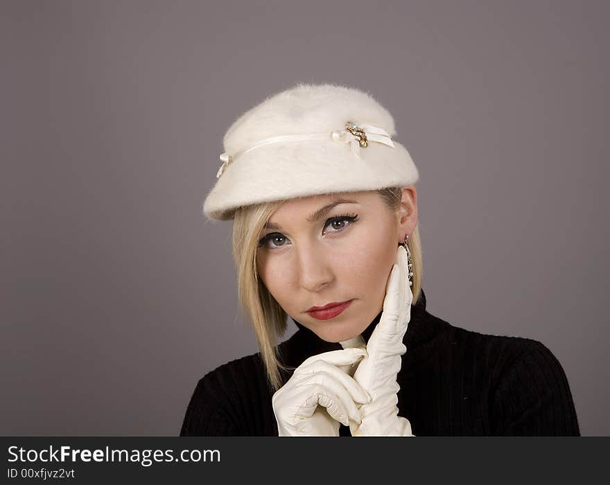 A blonde in a white fur hat and black turtleneck with her hand by her ear and earrings. A blonde in a white fur hat and black turtleneck with her hand by her ear and earrings