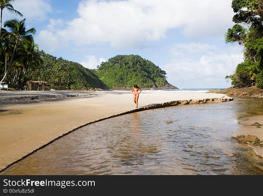 Beautiful woman walking along a river that runs towards the sea on a gorgeous tropical beach in Bahia state, Brazil. Beautiful woman walking along a river that runs towards the sea on a gorgeous tropical beach in Bahia state, Brazil.