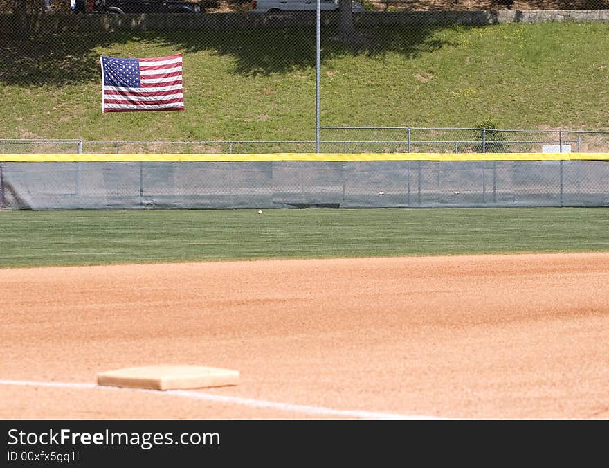 An outfield of a baseball or softball field with an American flag on the fence. An outfield of a baseball or softball field with an American flag on the fence