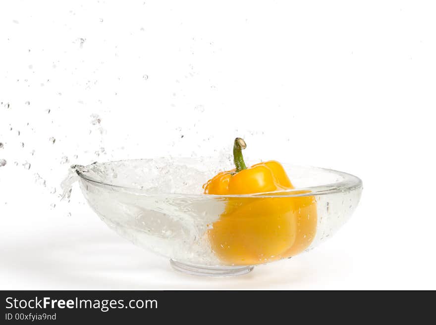 Yellow paprika falling into glass vase with water, splashes. Isolated over white