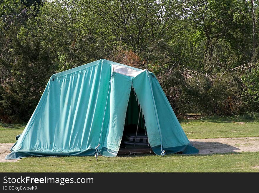 A blue tents on a green field with trees in the background.