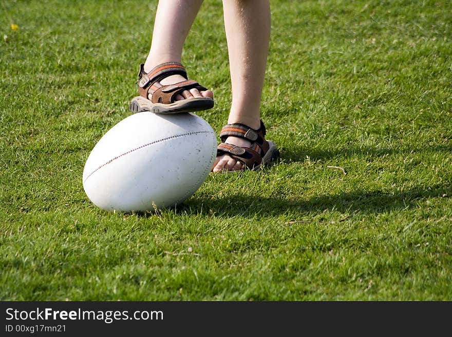 A young boy wearing sandals with a rugby ball on a grass field. A young boy wearing sandals with a rugby ball on a grass field.