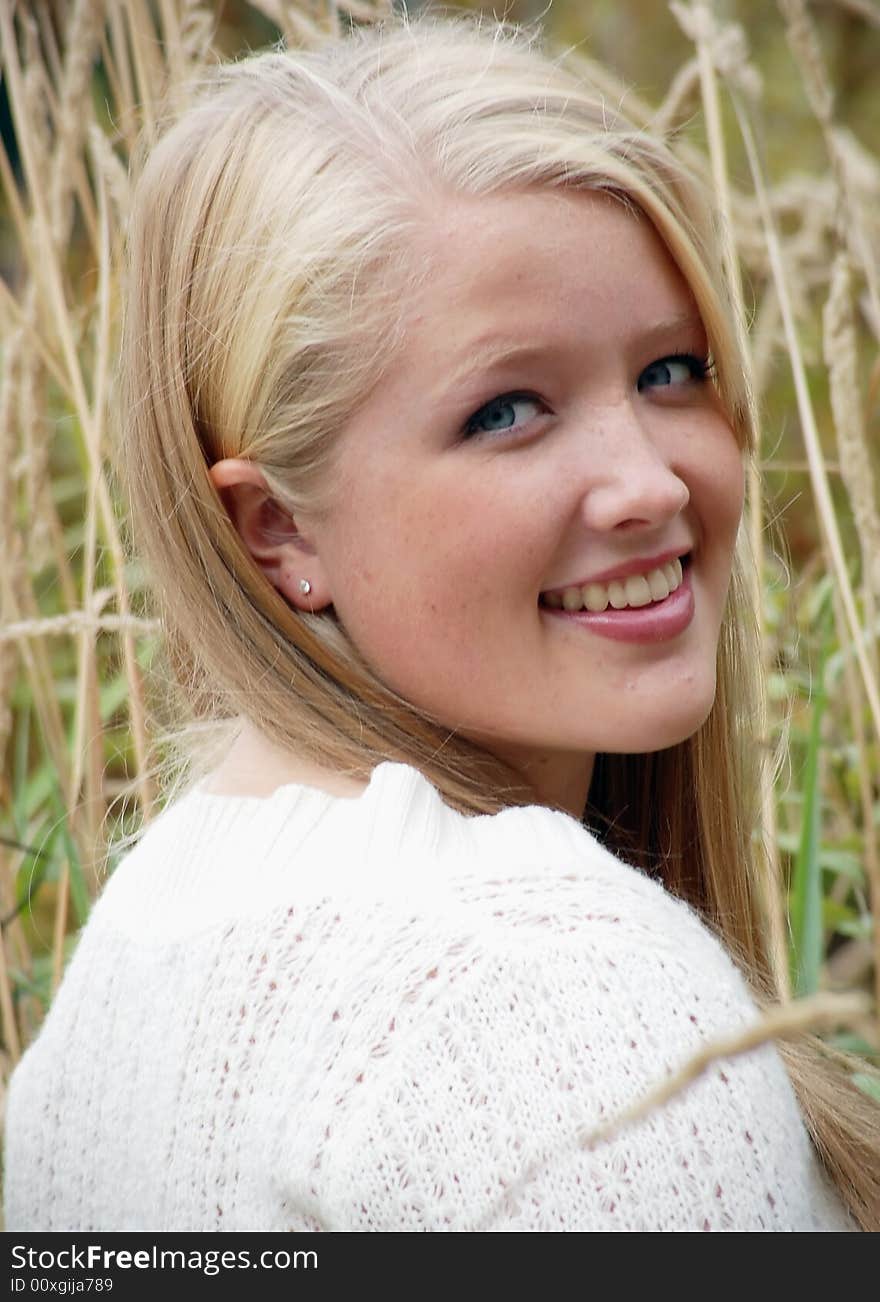 Attractive young blond woman sitting in the grass looking back over her shoulder at the camera. Vertically framed shot. Attractive young blond woman sitting in the grass looking back over her shoulder at the camera. Vertically framed shot.