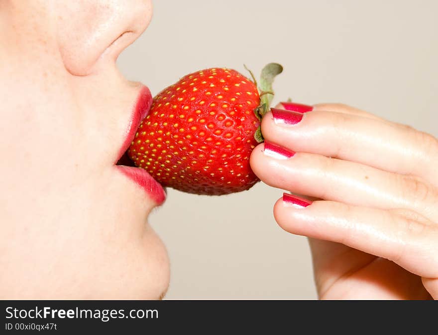 A girl, holding a strawberry between her red lips. A girl, holding a strawberry between her red lips