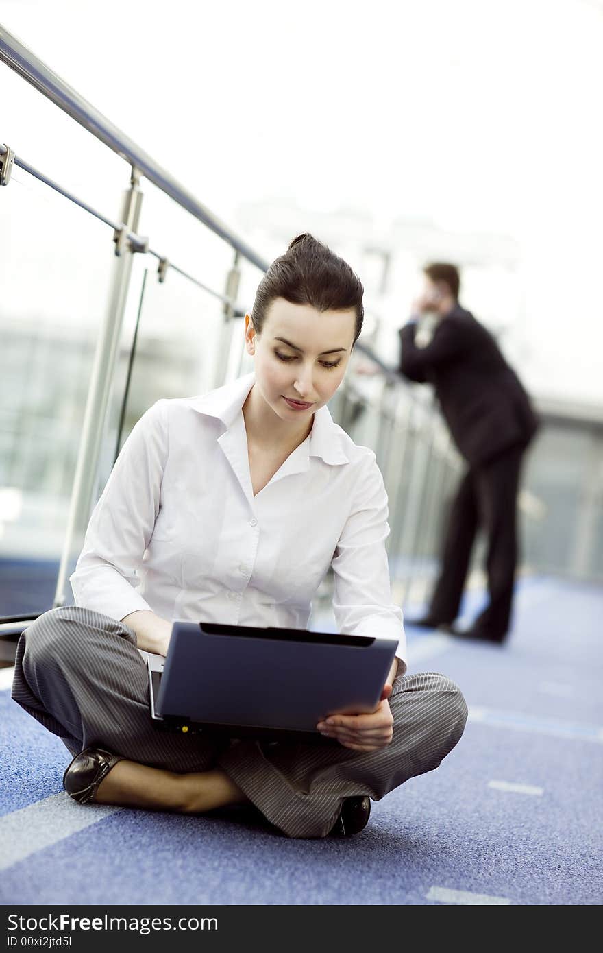 Portrait of young woman sitting with notebook on her lap in modern business office building corridor. Portrait of young woman sitting with notebook on her lap in modern business office building corridor