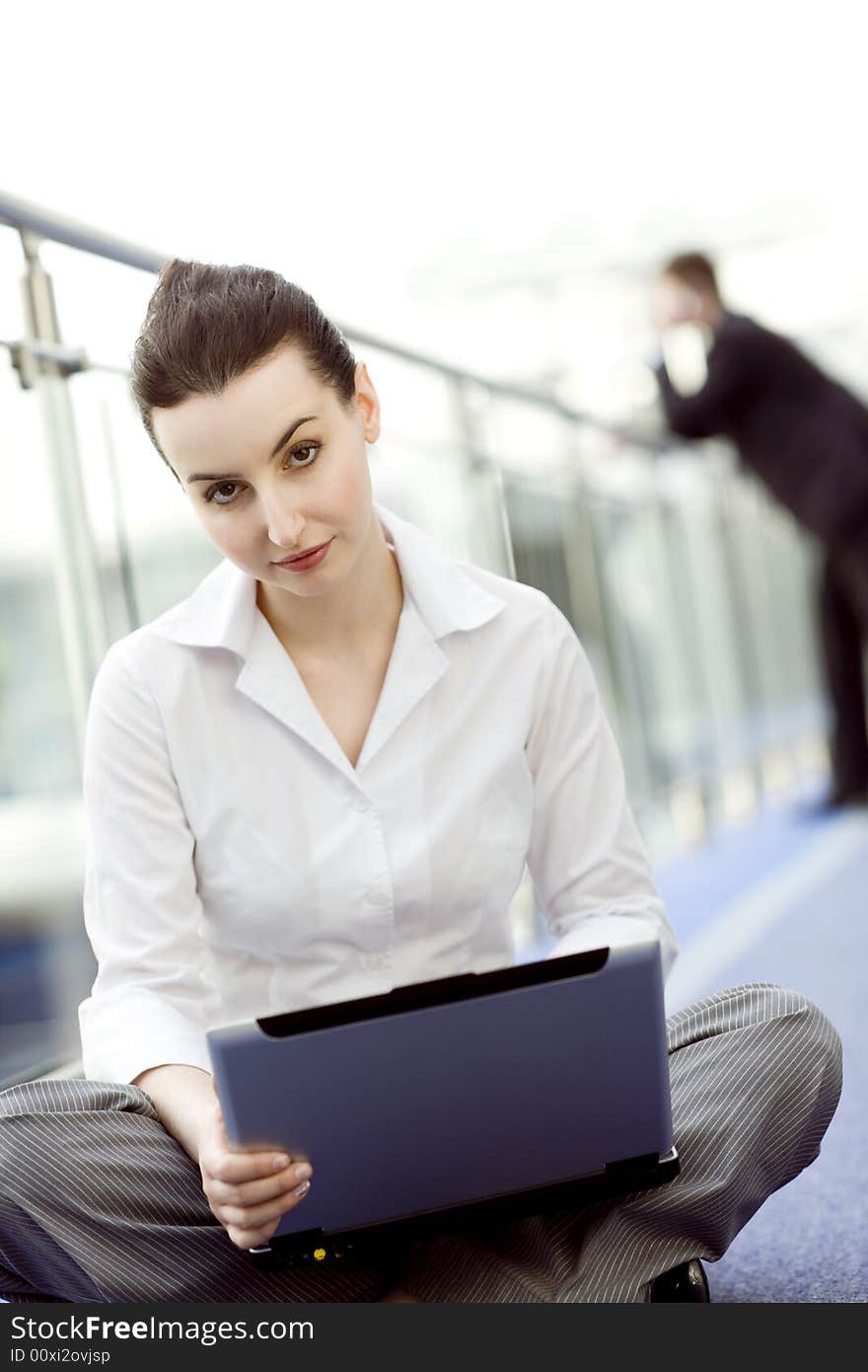 Portrait of young woman sitting with notebook on her lap in modern business office building corridor. Portrait of young woman sitting with notebook on her lap in modern business office building corridor