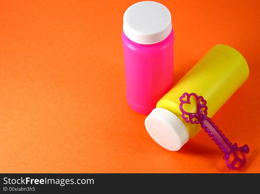 Two colorful bubble bottles and a blower, in orange background