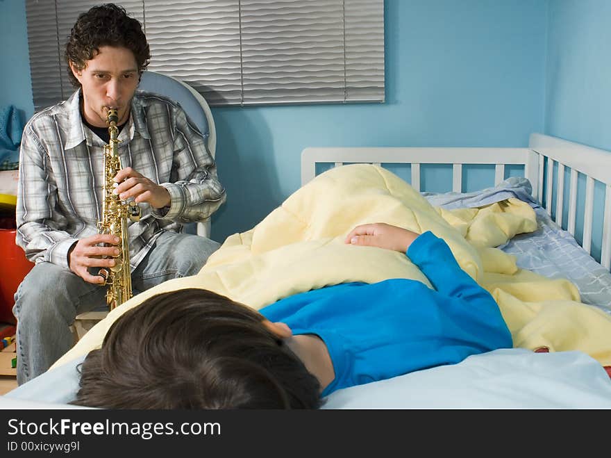 Young father playing a tune on a saxophone as his son gets ready to fall asleep. Young father playing a tune on a saxophone as his son gets ready to fall asleep