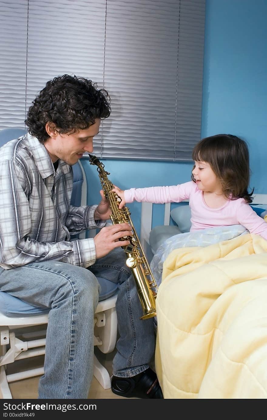 Little girl reaching out to grab her father's saxophone while he plays her a lullaby. Little girl reaching out to grab her father's saxophone while he plays her a lullaby