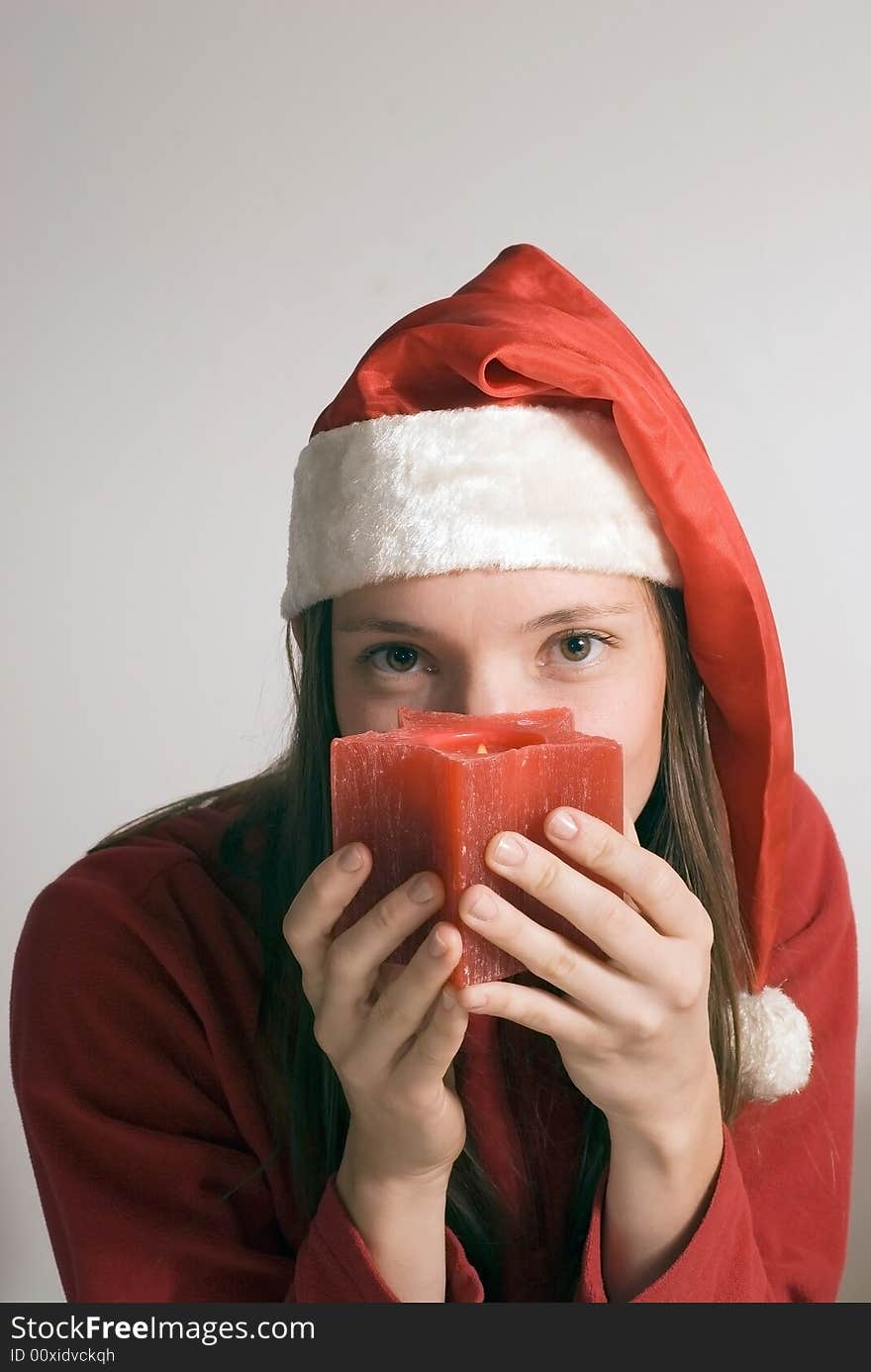 Vertically framed shot of an attractive woman in a santa hat looking seductively at the camera over a red candle. Vertically framed shot of an attractive woman in a santa hat looking seductively at the camera over a red candle