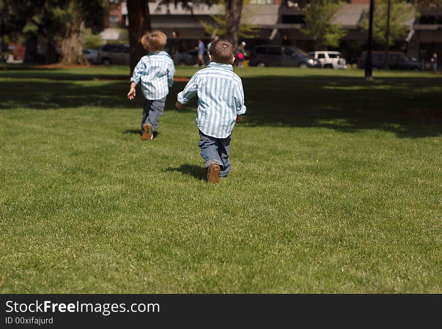 Outdoors shot of two young brothers running away from the camera, wearing identical button-up shirts and blue jeans. Outdoors shot of two young brothers running away from the camera, wearing identical button-up shirts and blue jeans.