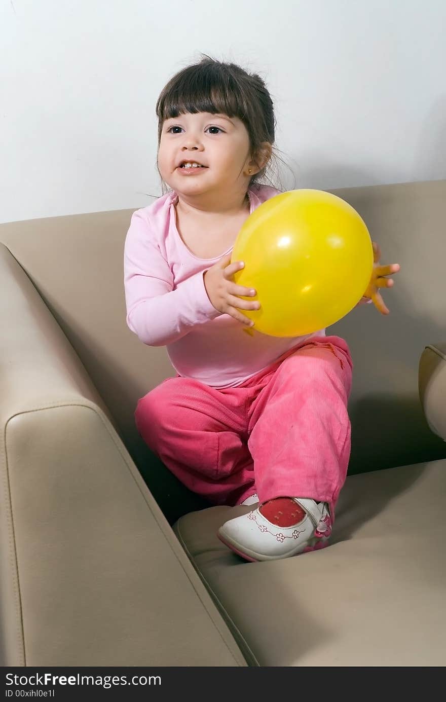 Cute young girl playing with a bright yellow balloon on a couch in her living room. Cute young girl playing with a bright yellow balloon on a couch in her living room