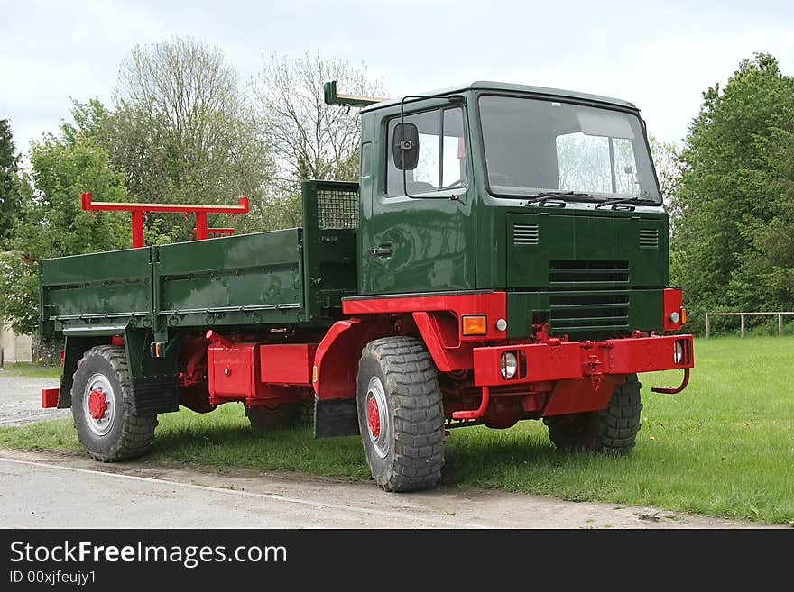 Old red and green truck with a tail gate, standing idle on the grass.