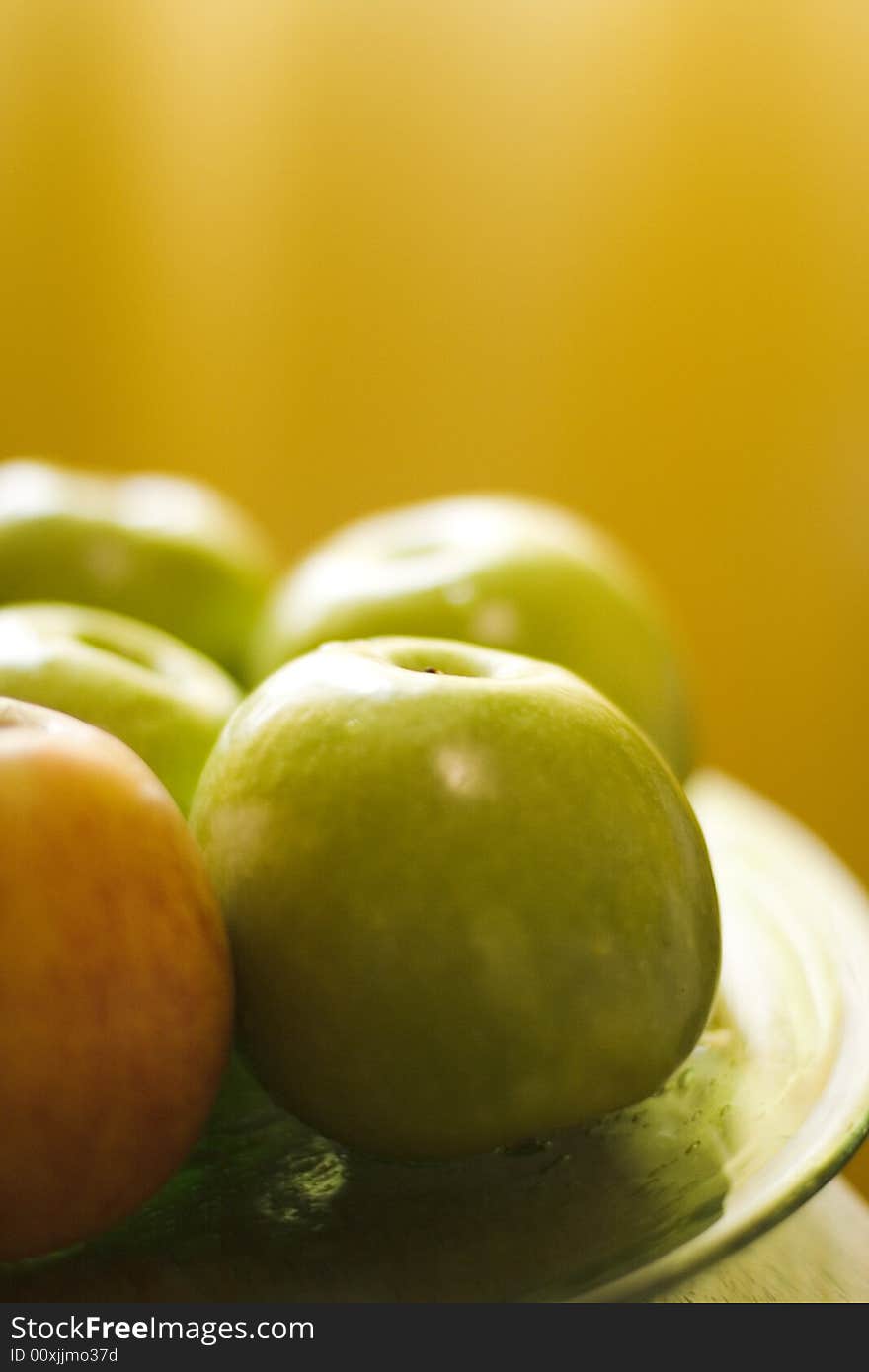 Four green apples and one red apples close-up on yellow background