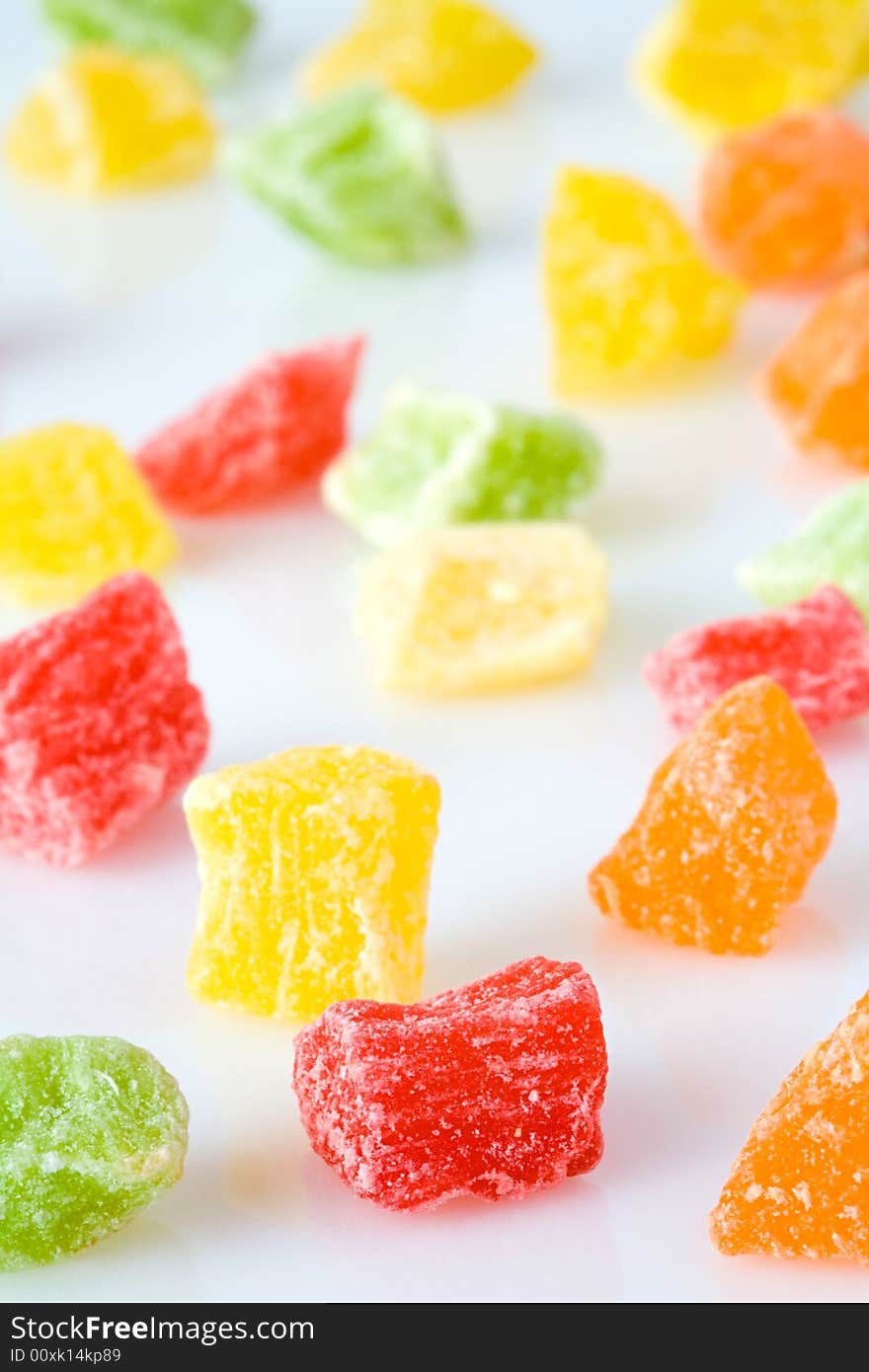 Small amount of the multi-coloured sweet dried fruits scattered on a white surface. Small amount of the multi-coloured sweet dried fruits scattered on a white surface