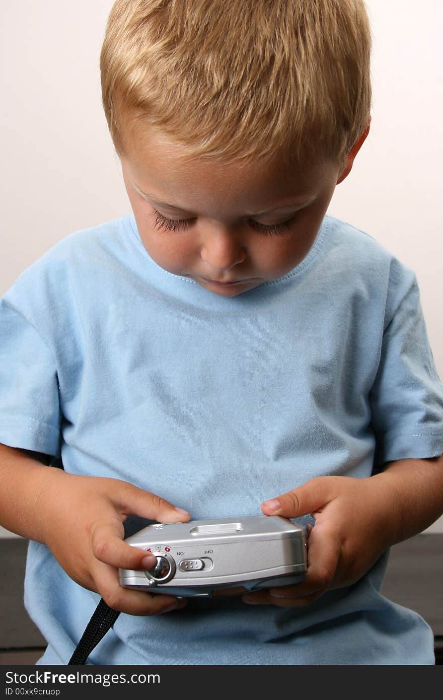 Shy toddler holding a silver camera, looking at his object. Shy toddler holding a silver camera, looking at his object