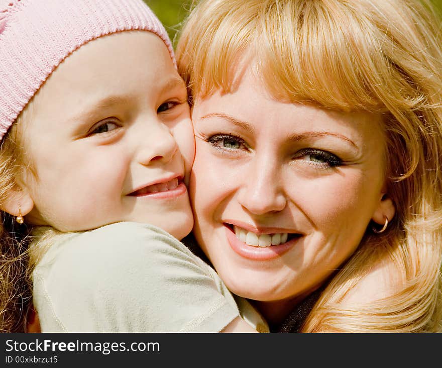 The beautiful little girl in a pink cap embraces mum with light hair. The beautiful little girl in a pink cap embraces mum with light hair