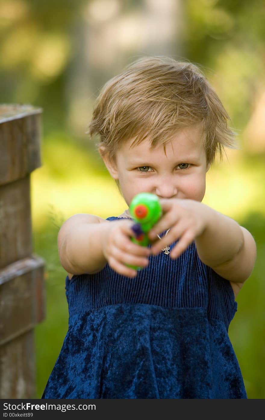 The little girl in a dark blue dress is going to shoot from a water pistol in summer day