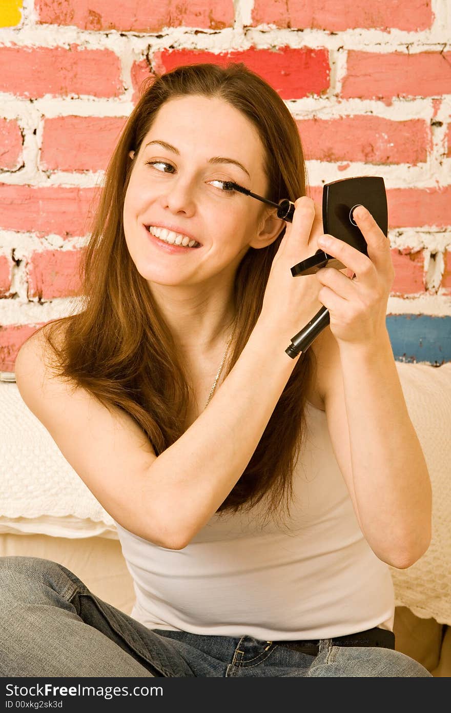 The girl paints eyelashes before a small pocket mirror. The girl paints eyelashes before a small pocket mirror