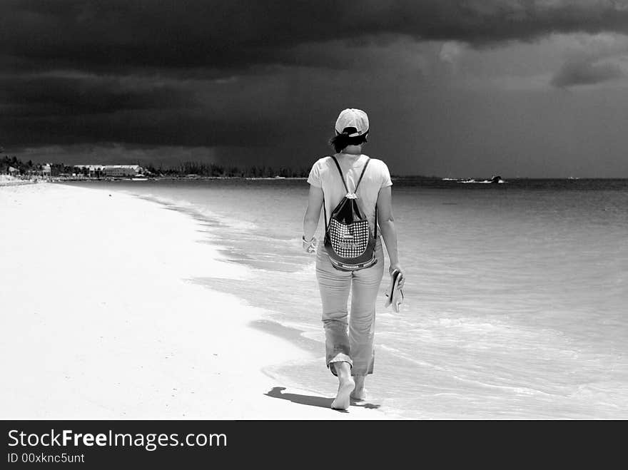 The girl walking on Our Lucaya beach with stormy dark clouds in a background on Grand Bahama Island, The Bahamas. The girl walking on Our Lucaya beach with stormy dark clouds in a background on Grand Bahama Island, The Bahamas.