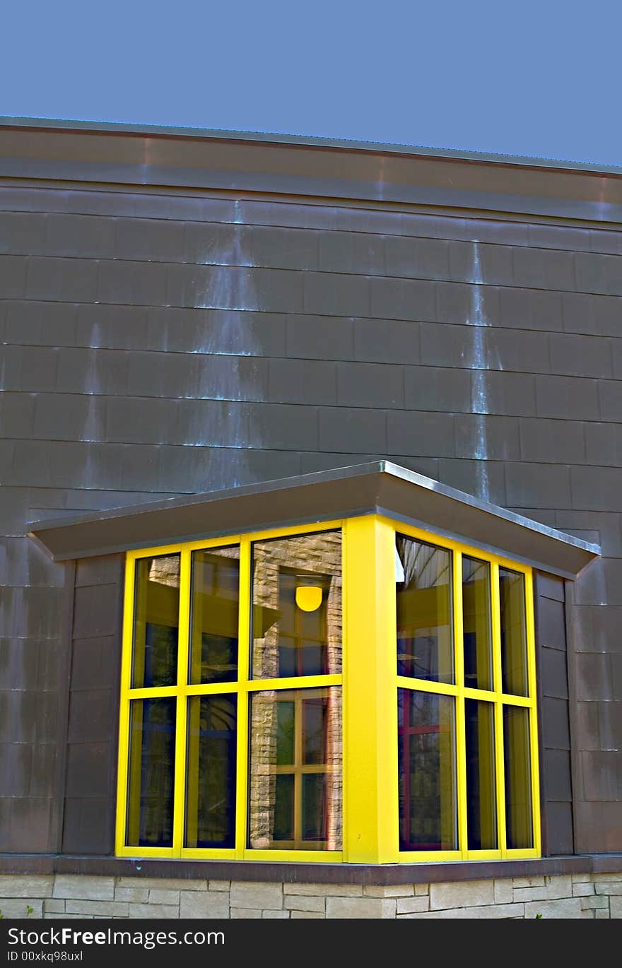 Close-up shot of a brown building with yellow window.  The sky is a solid blue above the building.  The building has some exterior effects from the weather.