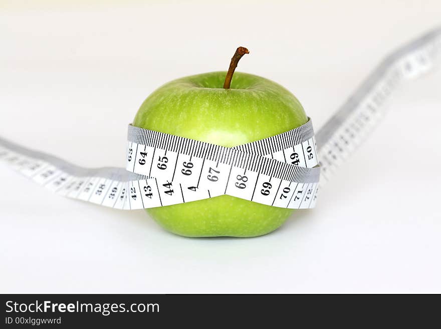 An green apple with a measuring tape around it on a white background. An green apple with a measuring tape around it on a white background.