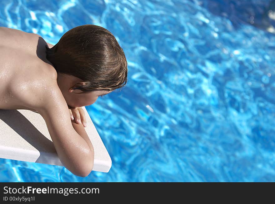 A boy looking into a pool from the diving board. A boy looking into a pool from the diving board