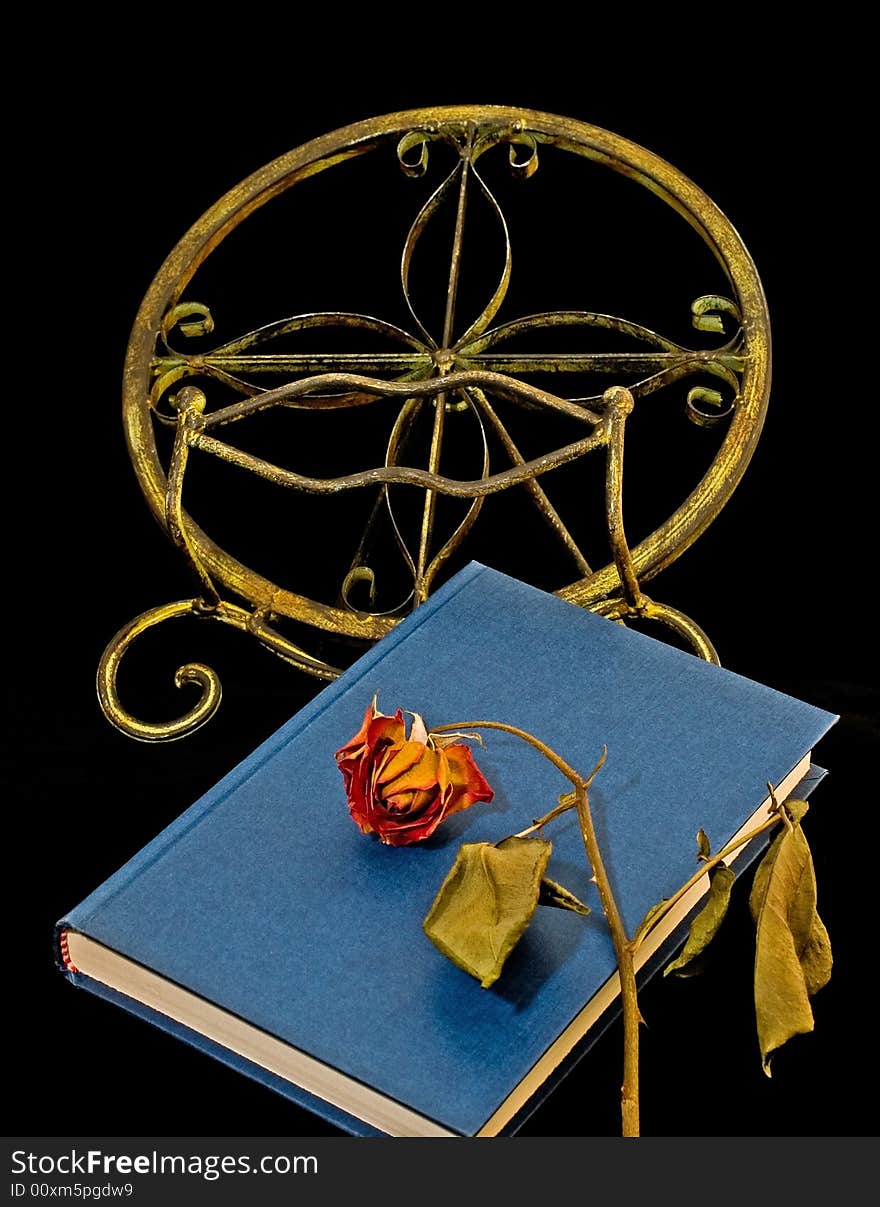 Dried-out rose on blue book and book-stand isolated on black. Dried-out rose on blue book and book-stand isolated on black