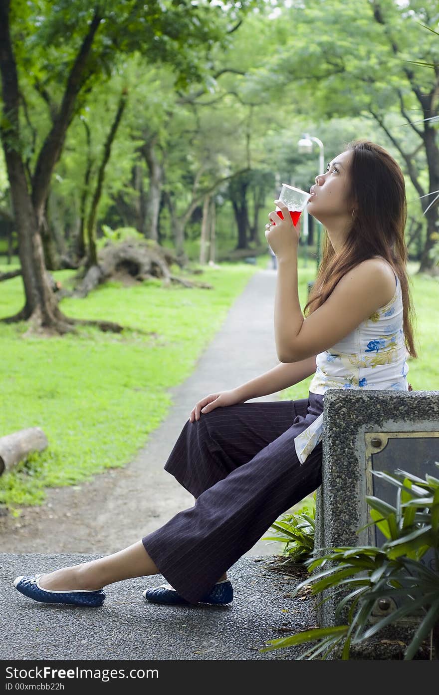 Beautiful woman about to drink a cup of red drinks while waiting along a long path to the woods. Beautiful woman about to drink a cup of red drinks while waiting along a long path to the woods