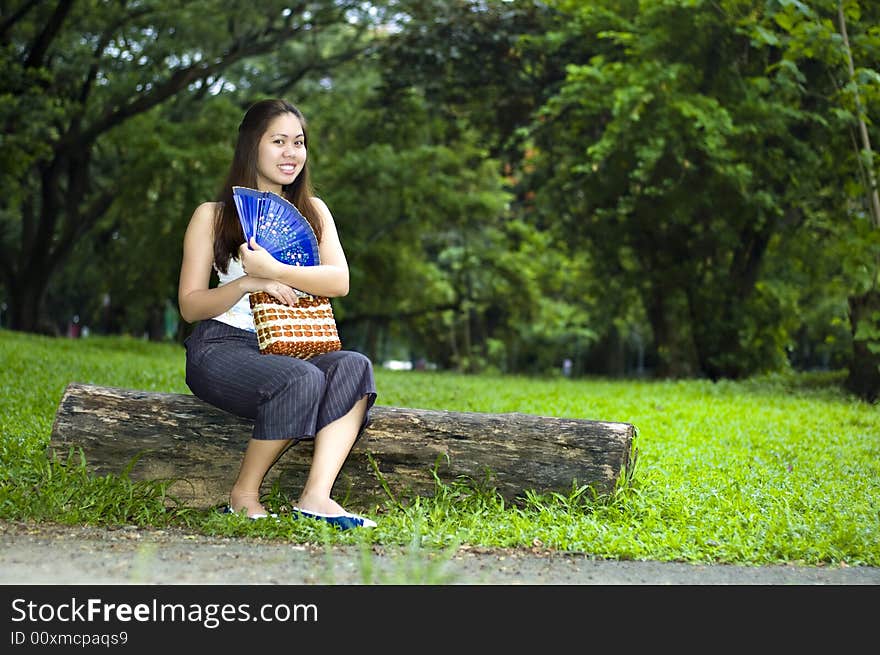 Asian woman showing off her blue chinese wooden fan with lush foilage at the background. Asian woman showing off her blue chinese wooden fan with lush foilage at the background.