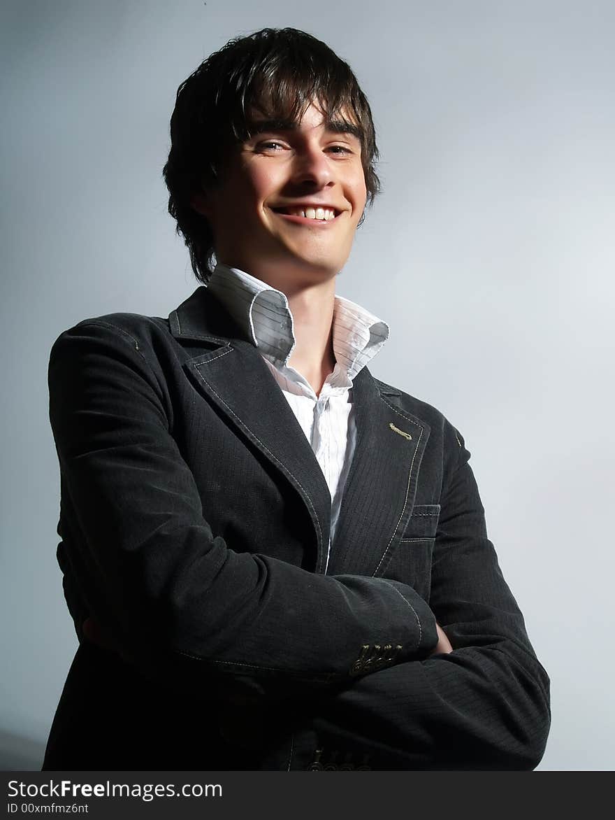 A portrait about a trendy attractive young man who is smiling and he has charming look. He is wearing a white shirt and a stylish black suit.