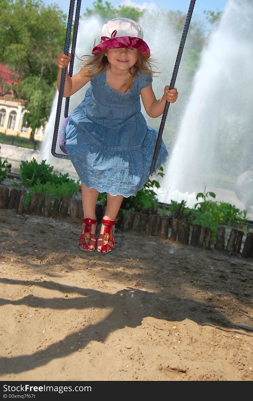 Little pretty swinging girl on the background of blue sky, trees and fountain. Little pretty swinging girl on the background of blue sky, trees and fountain