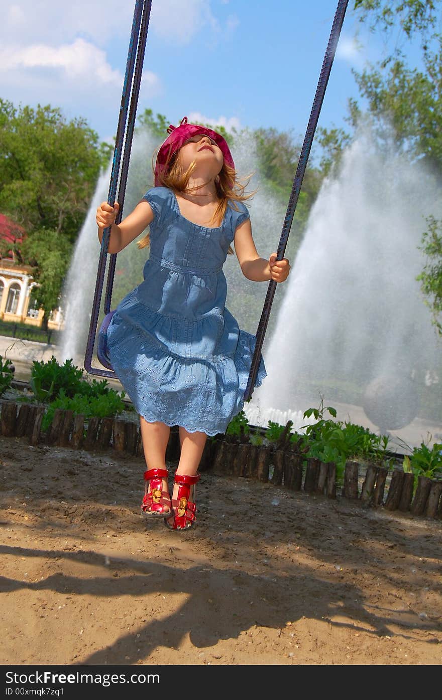 Little pretty swinging girl on the background of blue sky, trees and fountain. Little pretty swinging girl on the background of blue sky, trees and fountain