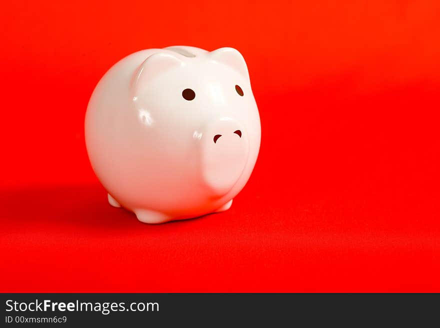 A white porcelain piggy bank on a red background with copy space. A white porcelain piggy bank on a red background with copy space