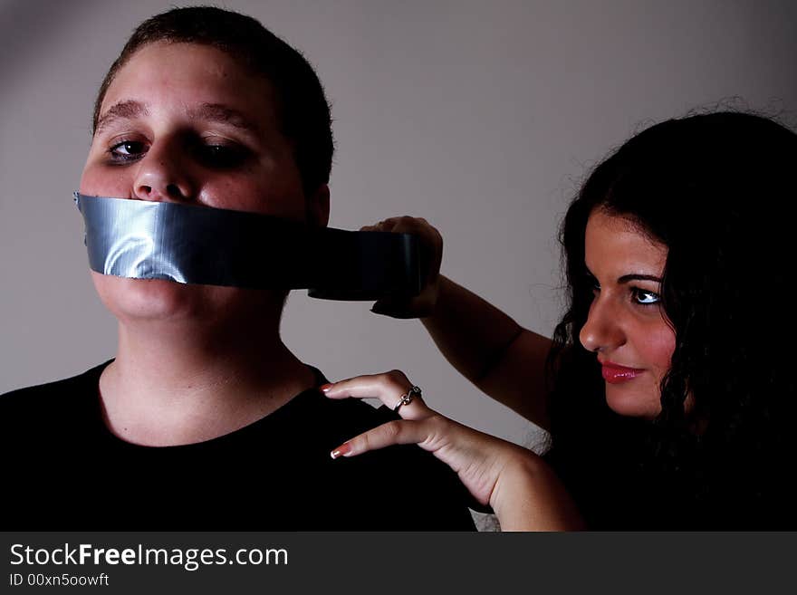 Woman taping a mans mouth with duct tape.