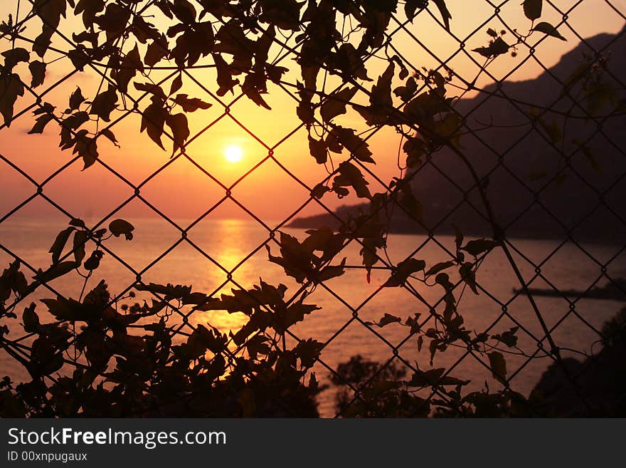 A sunset on the sea and a mountain behind the grid. A sunset on the sea and a mountain behind the grid