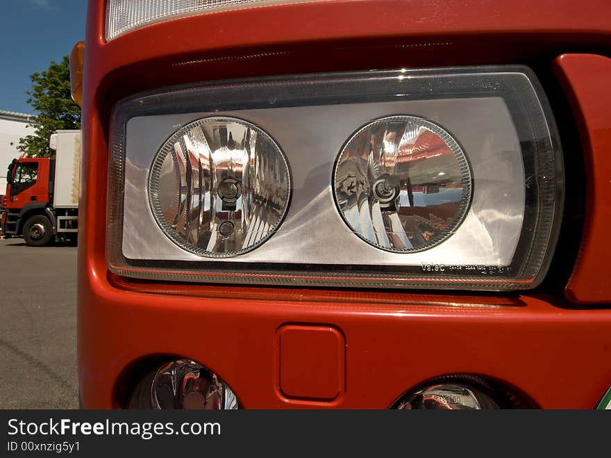 The headlamp of truck and in the background another truck. The headlamp of truck and in the background another truck