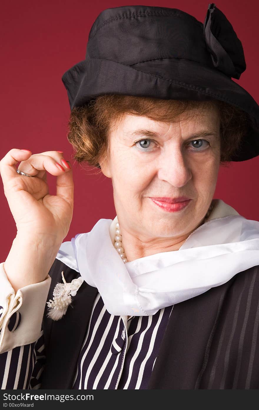 The elderly woman in a hat on a red background. The elderly woman in a hat on a red background.